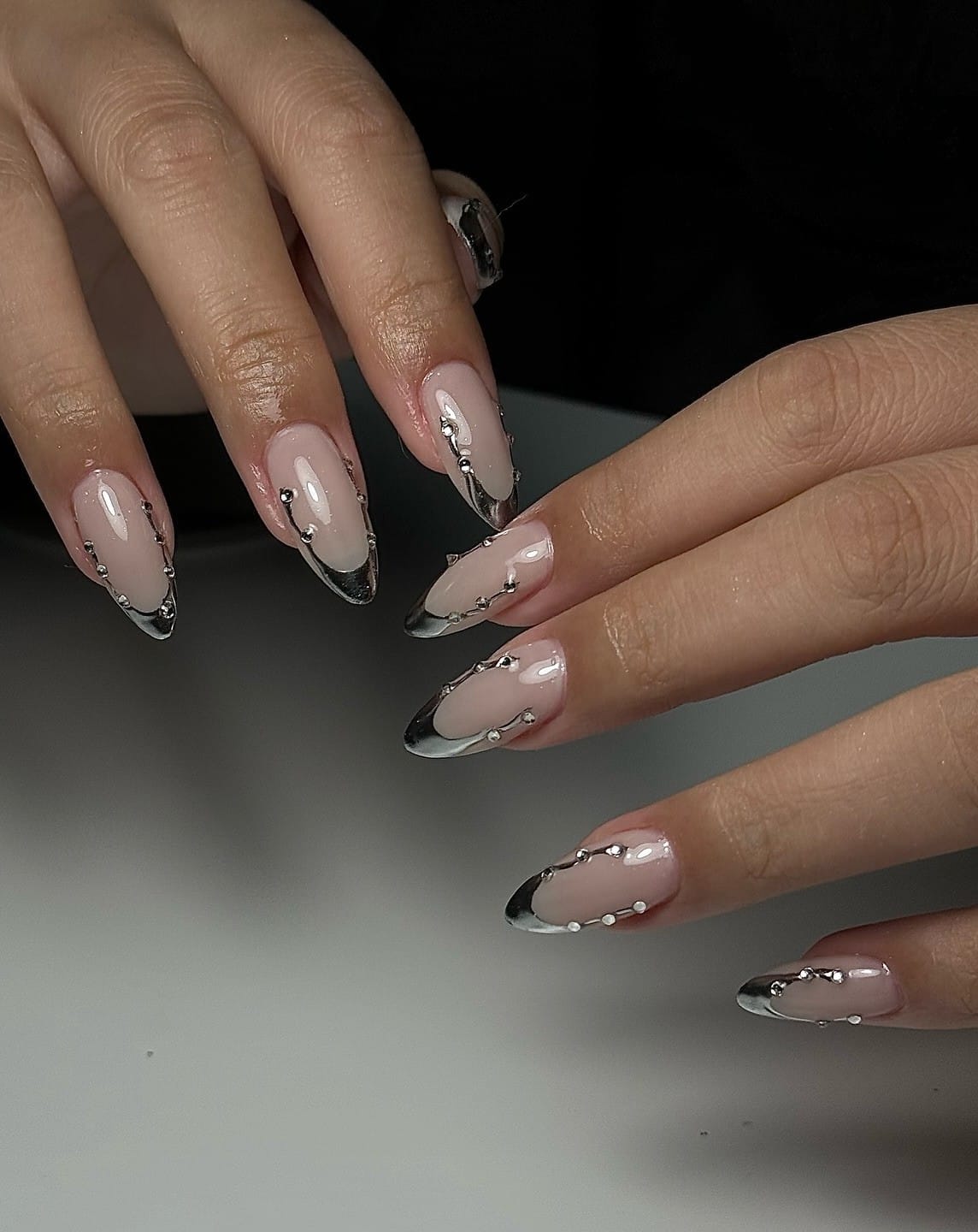 Almond fall nails with silver chrome French tips and 3D chrome drips set with tiny gems on a nude base