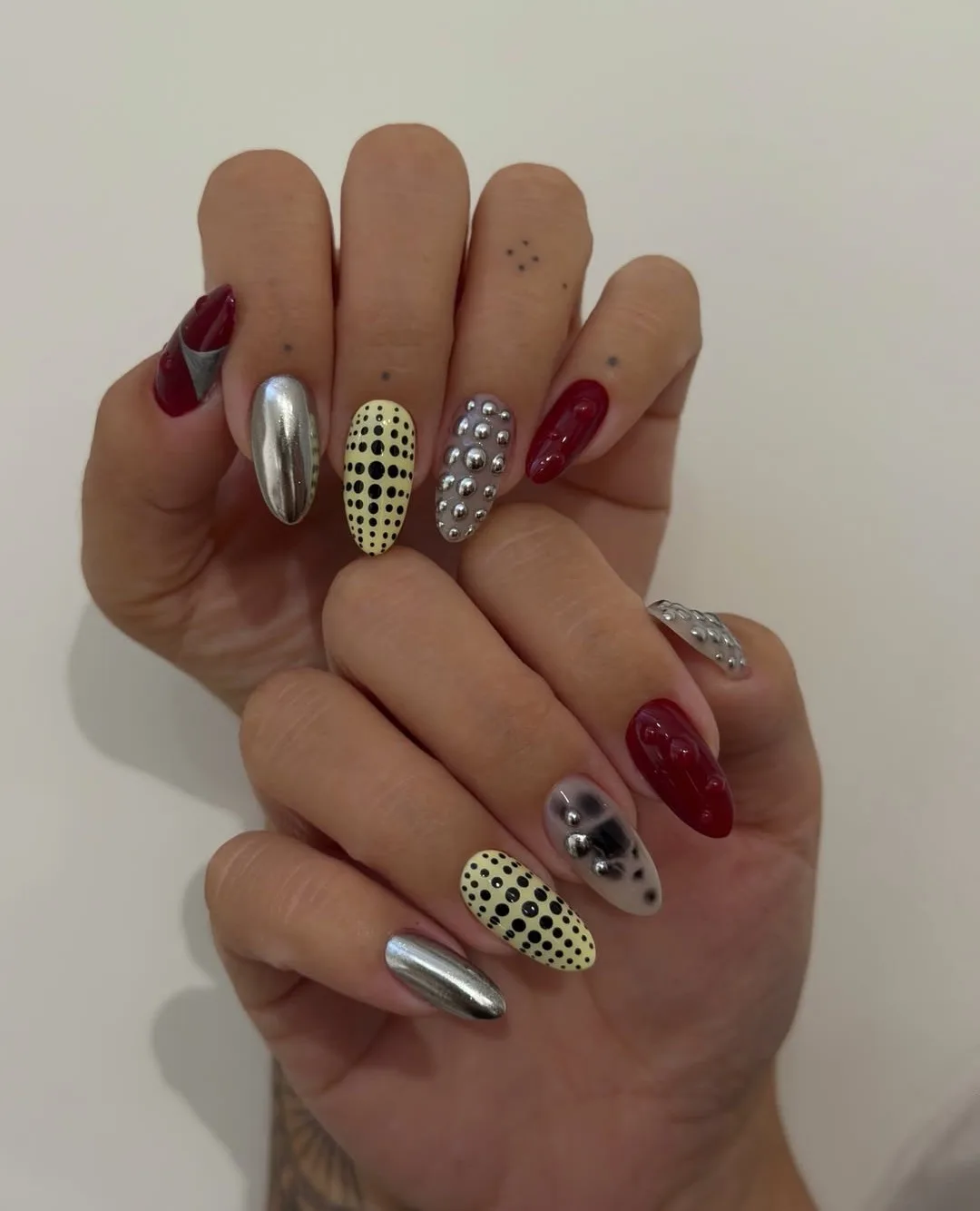 Almond autumn nails mixing silver chrome, silver studs, deep red 3D drops, and a yellow and black dot accent