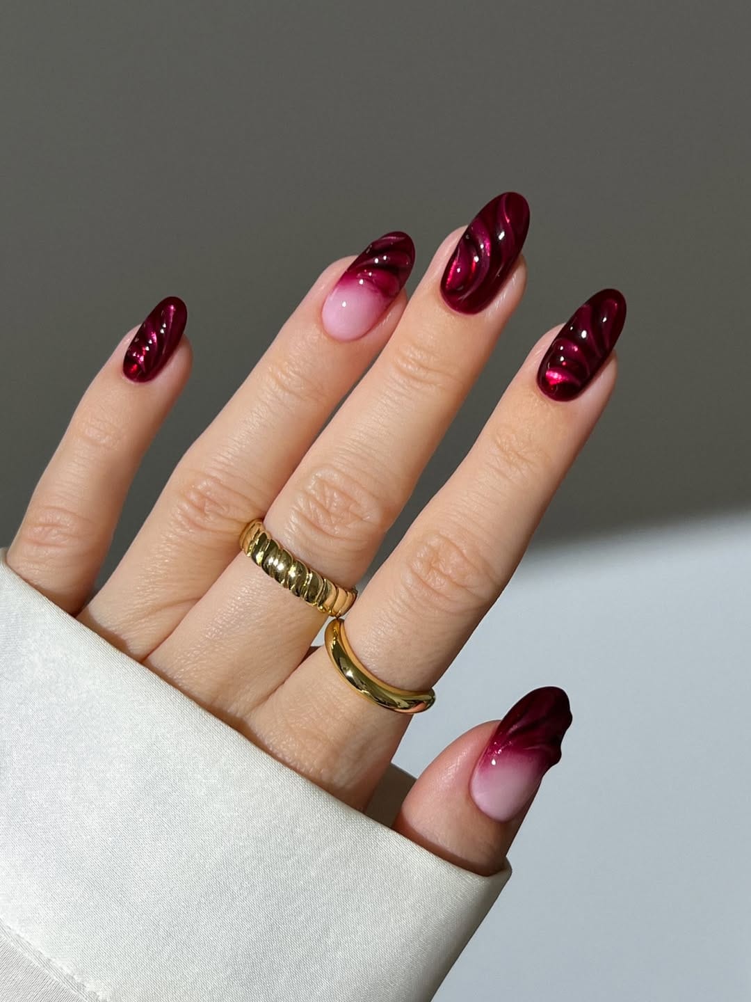 Oval November nail colors in cranberry cat-eye swirls with two pink ombre accent nails