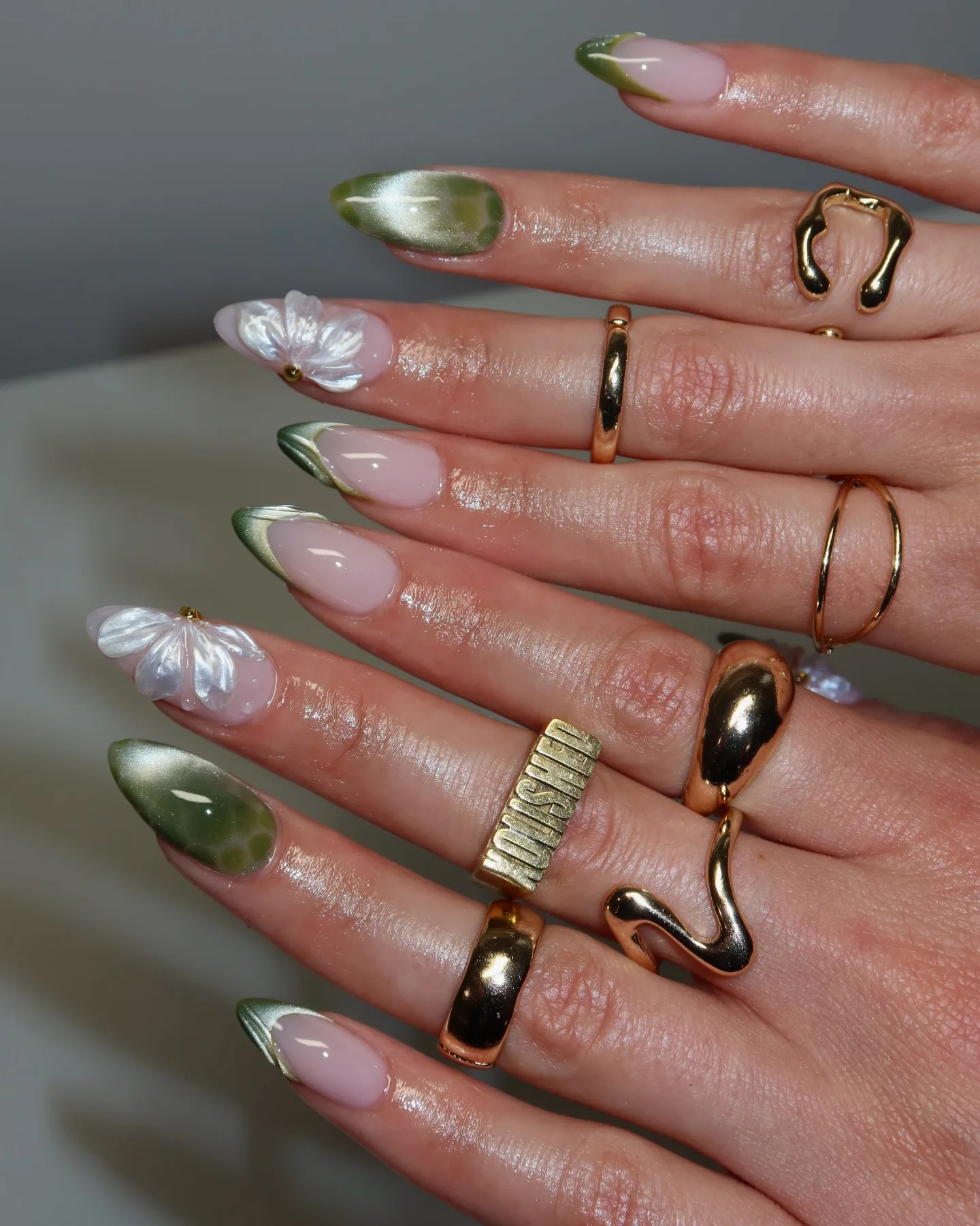 Almond fall nails mixing olive green cat-eye, green chrome French tips, and pearly 3D flower accents