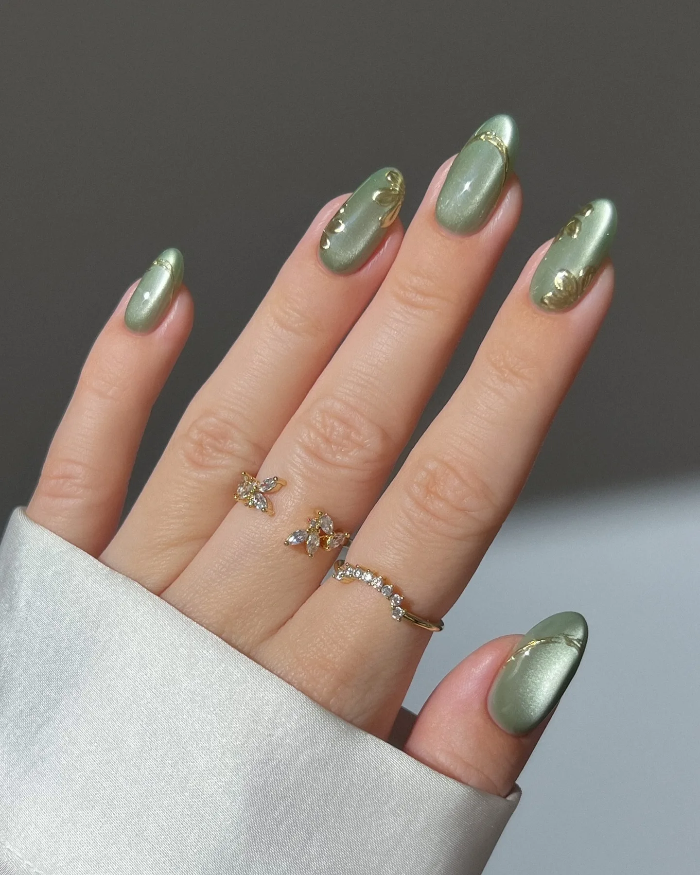 Almond autumn nails in sage green cat-eye polish with gold foil leaf and line accents