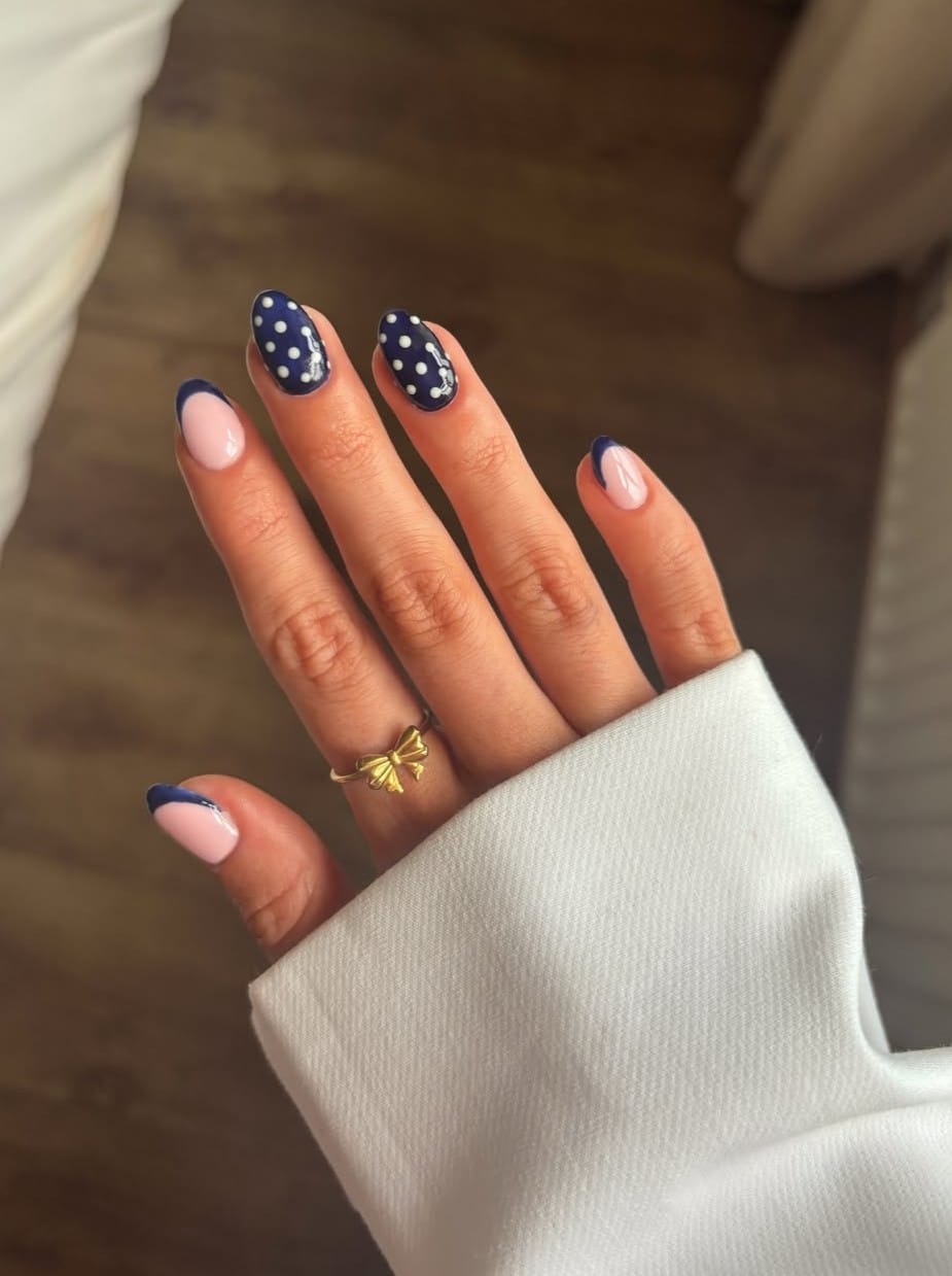 Short oval fall nails with navy polka dot accents and navy curved French tips on a pink base