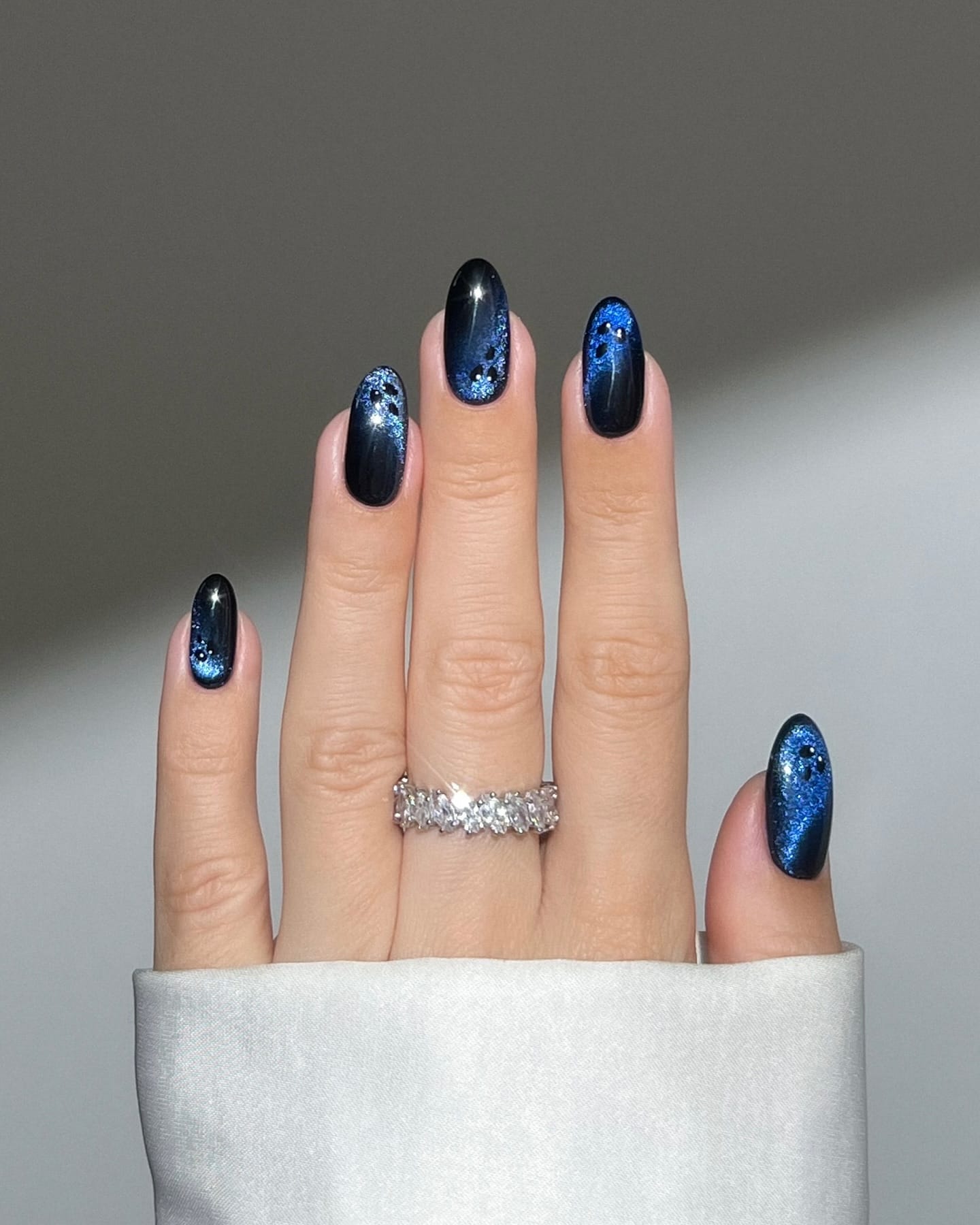 Almond autumn nails in black with a deep blue cat-eye shimmer and small black dot details