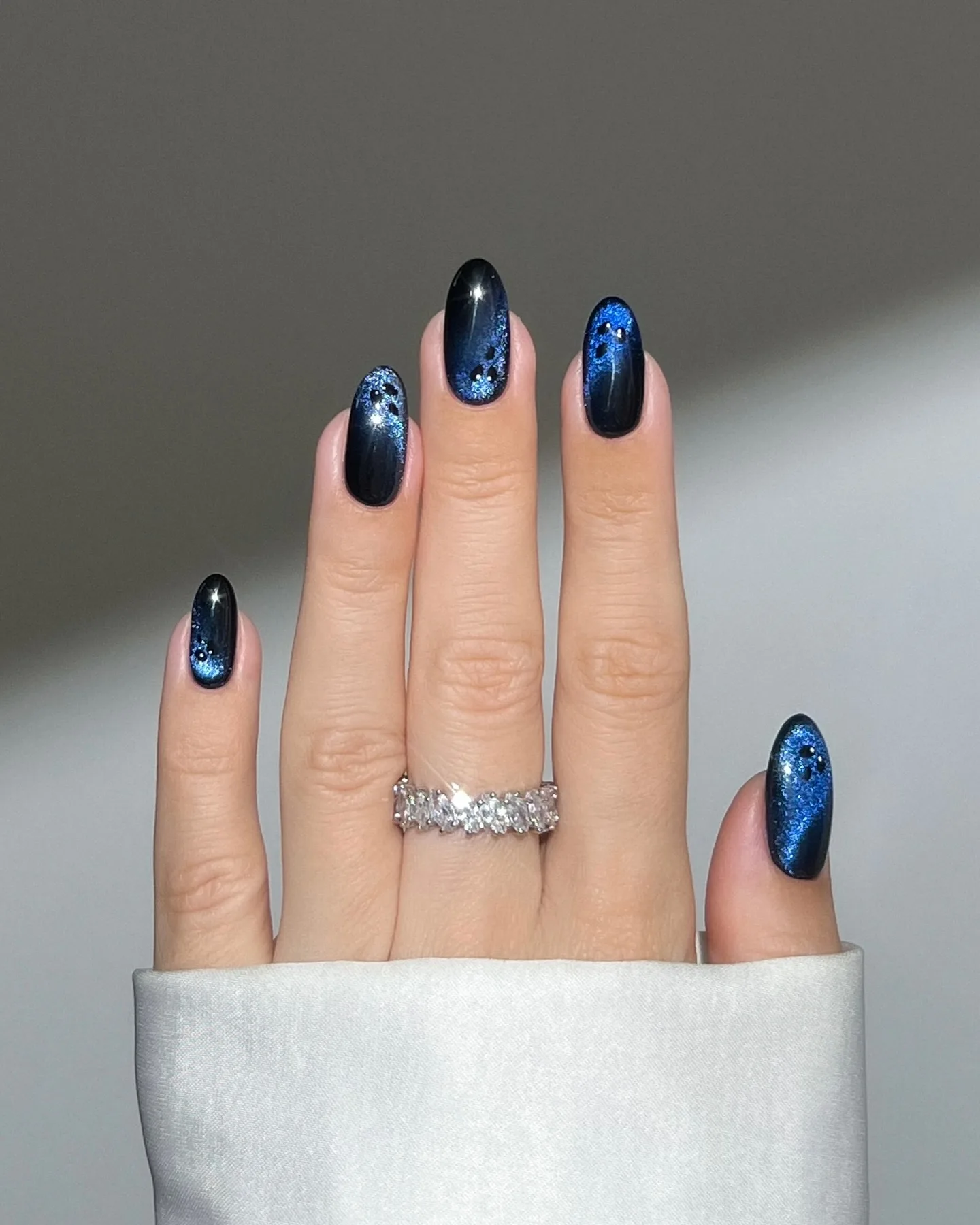Almond autumn nails in black with a deep blue cat-eye shimmer and small black dot details