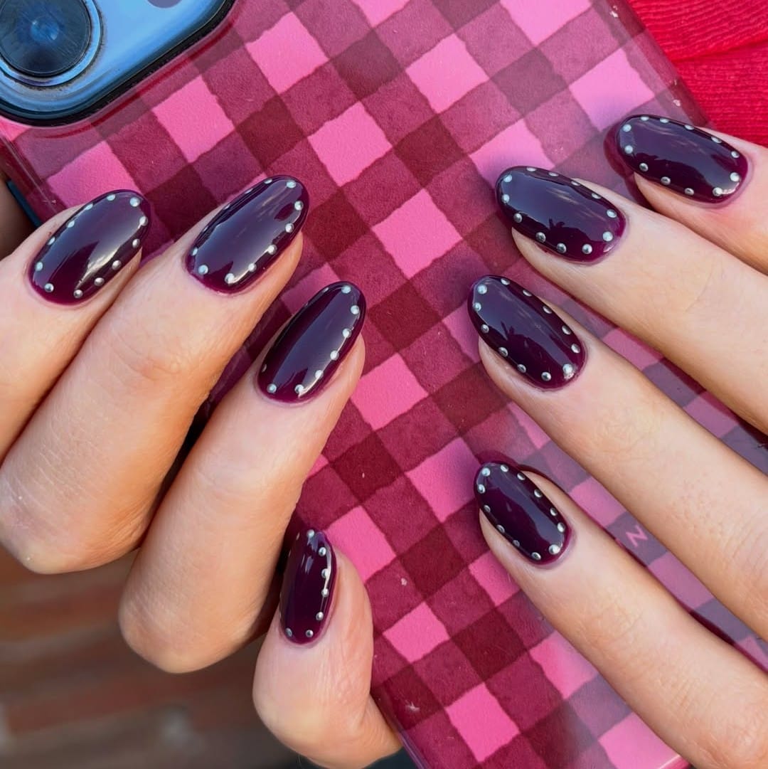 Oval November nail colors in dark blackberry plum outlined with tiny silver studs
