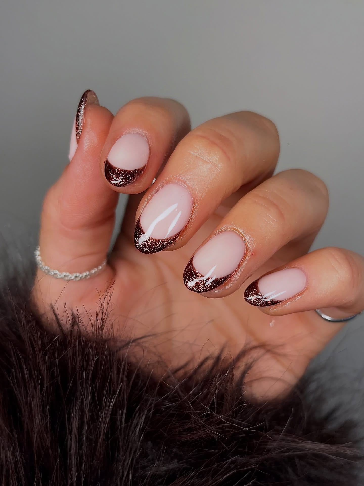 Short oval fall nails with a sheer pink base and shimmery chocolate brown glitter French tips
